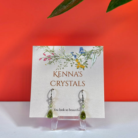 Teardrop peridot earrings with silver hooks on a floral Kenna's Crystals display card.