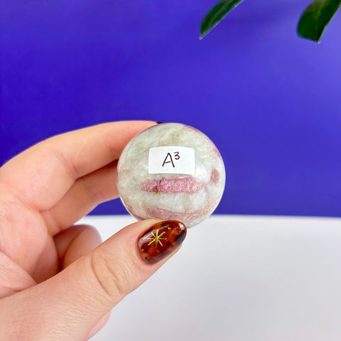 Polished petrifying pink tourmaline sphere with white quartz inclusions held in a hand against a blue background.