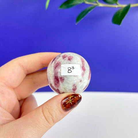 Polished pink tourmaline sphere with white quartz matrix held in hand against a blue background.