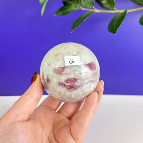 Polished pink tourmaline sphere with vibrant magenta inclusions held in a hand against a blue background.