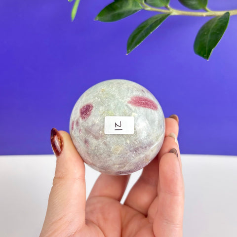 Polished pink tourmaline sphere with natural inclusions held in a hand against a blue and white background.