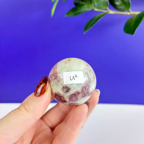 Polished pink tourmaline sphere with white inclusions held in a hand against a blue background.