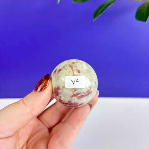 Polished pink and green tourmaline sphere held in hand against a blue background.