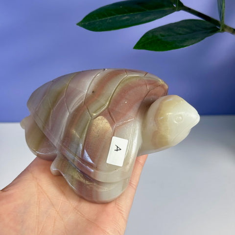 Pink banded onyx turtle figurine, variant A, held in a hand.