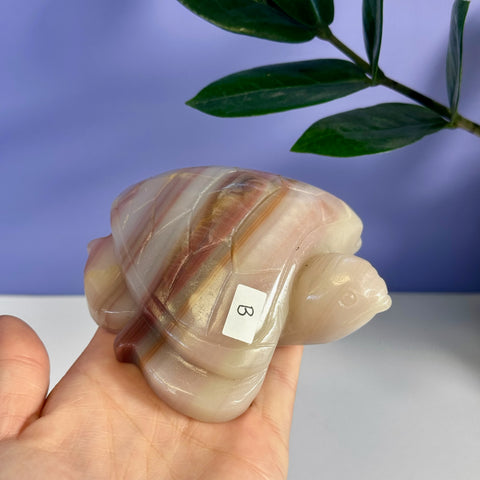 Pink banded onyx turtle carving with natural white and brown stripes, held in a hand.