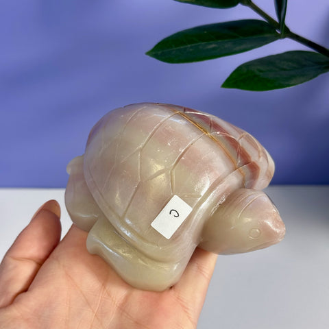 Pink banded onyx turtle figurine with carved shell details, held in a hand.