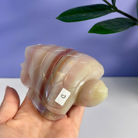 Pink banded onyx turtle carving, variant D, held in a hand.