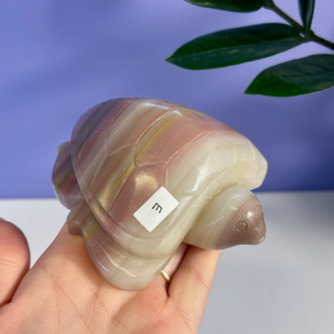 Pink banded onyx turtle carving, variant E, held in a hand.