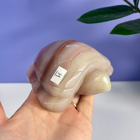 Pink banded onyx turtle carving with smooth, polished finish, held in a hand.