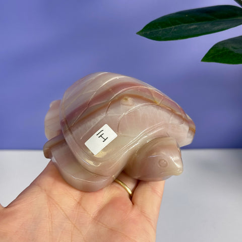 Pink banded onyx turtle carving with smooth, polished finish, held in a hand.