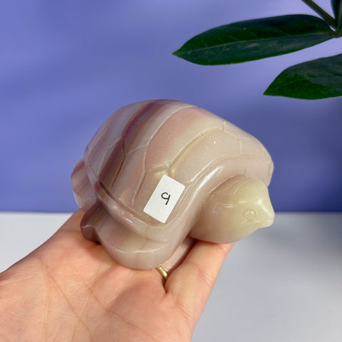Pink banded onyx turtle carving with subtle stripes, held in a hand.