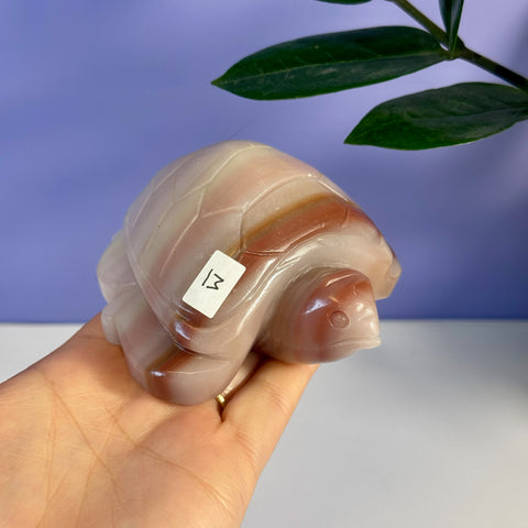 Hand-held pink banded onyx turtle carving with natural reddish-brown stripes and a smooth finish.