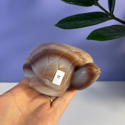 Hand holding a carved pink banded onyx turtle with natural brown and white stripes.