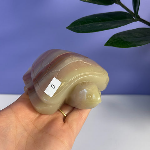 Pink banded onyx turtle carving with natural striations, held in a hand.