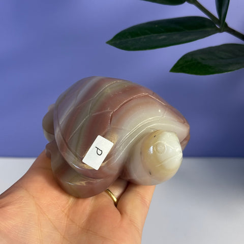 Pink banded onyx turtle carving with white and brown stripes, held in a hand.