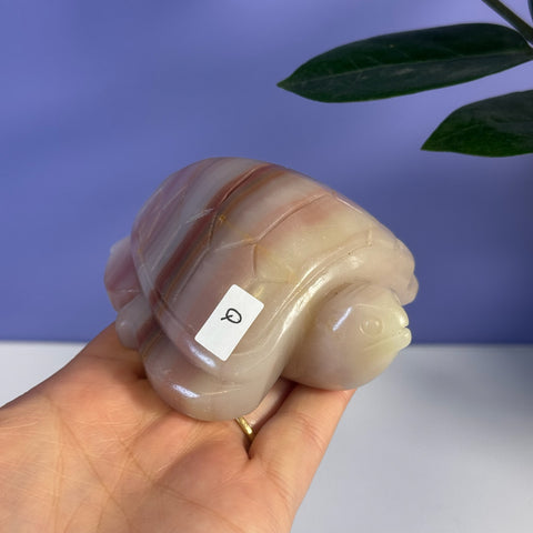 Pink banded onyx turtle carving with a Q sticker, held in a hand.