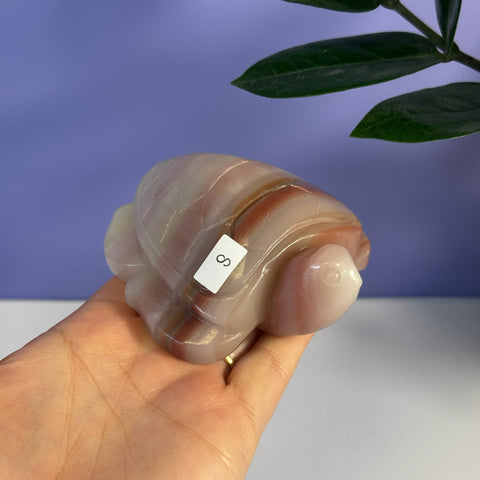 Pink banded onyx turtle carving held in a hand, showcasing its smooth, polished finish and natural striped patterns.