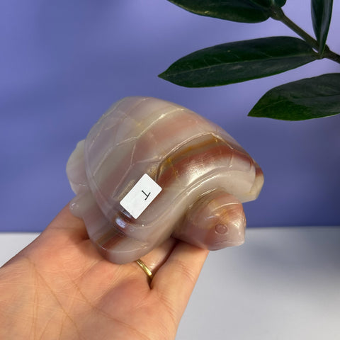 Pink banded onyx turtle carving with natural white and brown stripes, held in a hand.