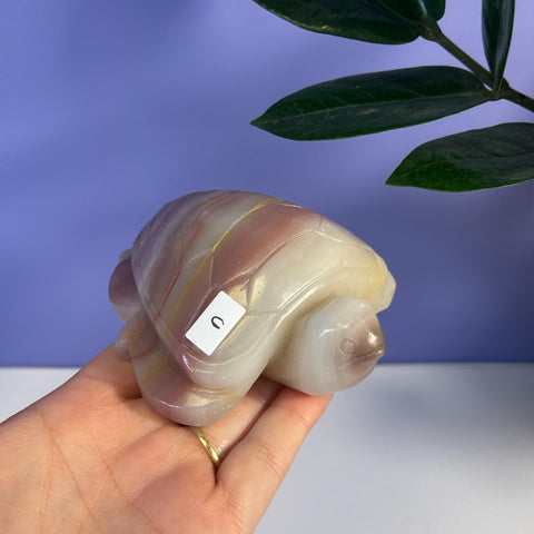 Pink banded onyx turtle figurine, held in a hand, with a "U" sticker on its shell.