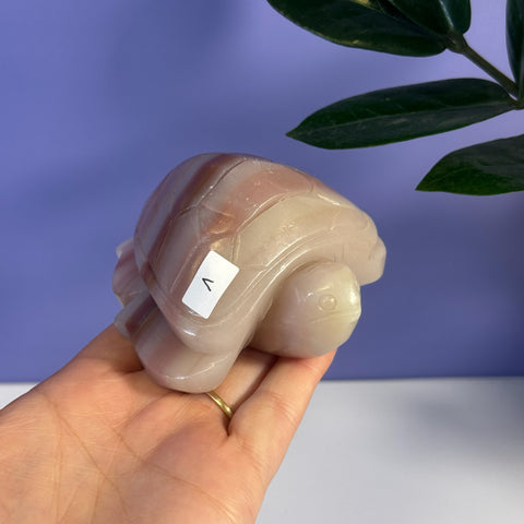 Hand-held pink banded onyx turtle carving with a smooth, polished finish.