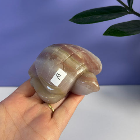 Pink banded onyx turtle carving with natural striations, held in a hand.