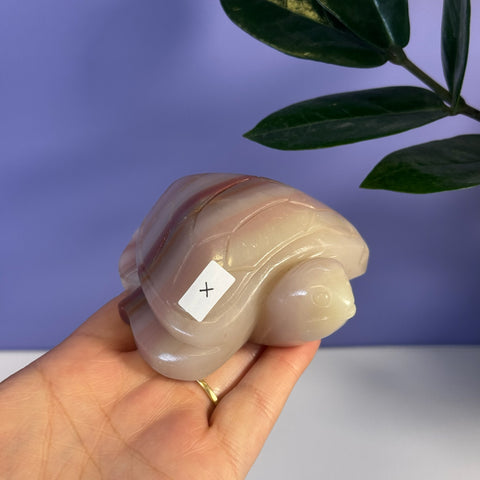 Pink banded onyx turtle carving held in a hand, showcasing its smooth, polished finish and natural stone patterns.