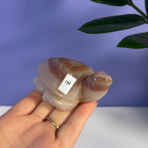 Hand holding a pink banded onyx turtle carving with natural striations.