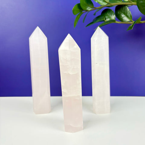 Three polished pink calcite crystal towers standing upright against a vibrant purple background.