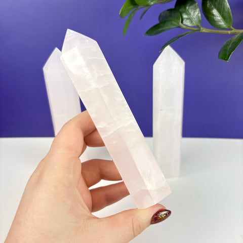 Hand holding a translucent, pale pink calcite crystal tower with two additional towers in the background.