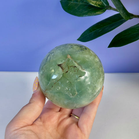 Hand holding a smooth, pale green Prehnite sphere with a unique natural star-shaped inclusion.