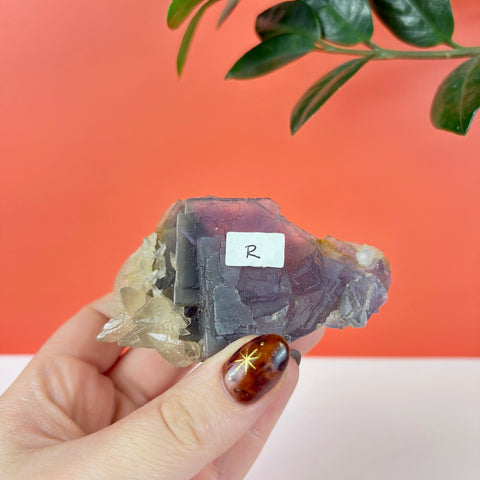 Hand held raw purple prism fluorite crystal cluster with geometric cubic structure and clear quartz accents.
