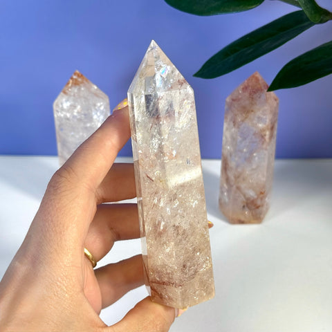 Hand holding a tall, clear Rainbow Pink Fire Azeztulite crystal tower with subtle pink and red inclusions.