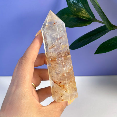 Hand holding a clear Rainbow Pink Fire Azeztulite crystal tower with orange and red inclusions.
