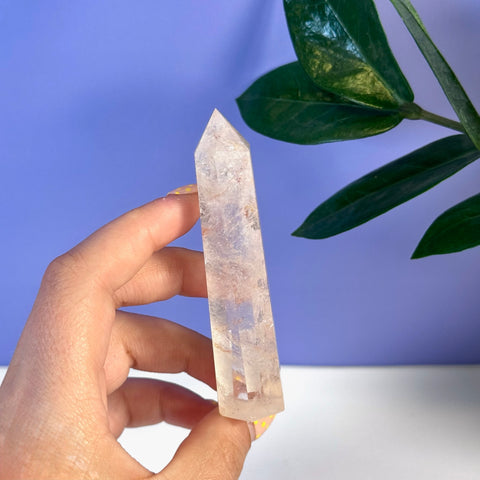 Hand holding a clear, pointed Rainbow Pink Fire Azeztulite crystal tower with subtle pink and rainbow hues.