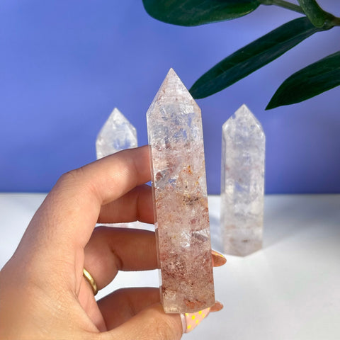 Hand holding a clear Rainbow Pink Fire Azeztulite crystal tower with red inclusions.