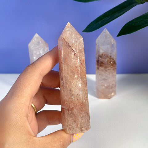 Hand holding a pink fire azeztulite crystal tower with rainbow inclusions.
