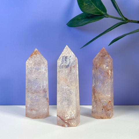 Three clear crystal towers with pink and red inclusions, standing on a white surface against a purple background.