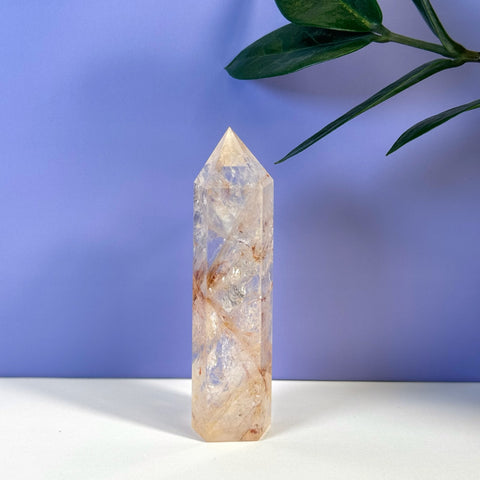 Rainbow Pink Fire Azeztulite Tower, a clear crystal with pink and orange inclusions, on white.
