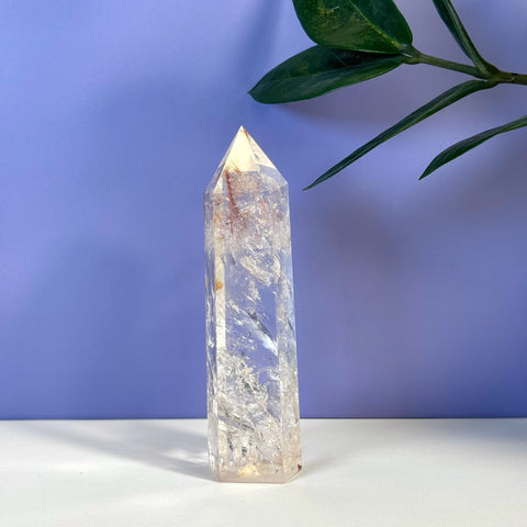 Rainbow Pink Fire Azeztulite crystal tower with clear, pink, and orange hues on a purple background.