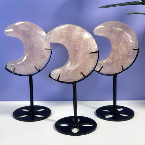 Three pink rose quartz crescent moons on black stands.