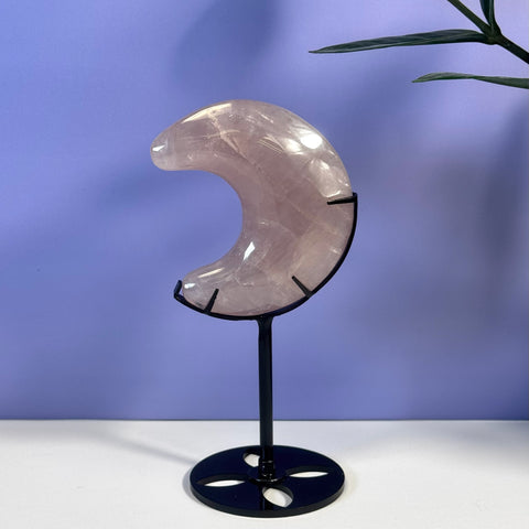 Rose Quartz Crescent Moon with black metal stand, set against a purple background.