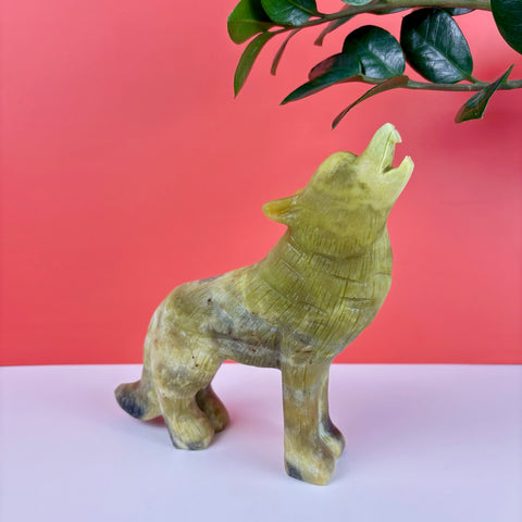 Hand-carved light green serpentine stone wolf figurine howling, featuring detailed fur textures against a red background.