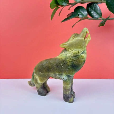 Hand-carved green serpentine stone wolf figurine in a howling pose with detailed fur texture against a coral background.