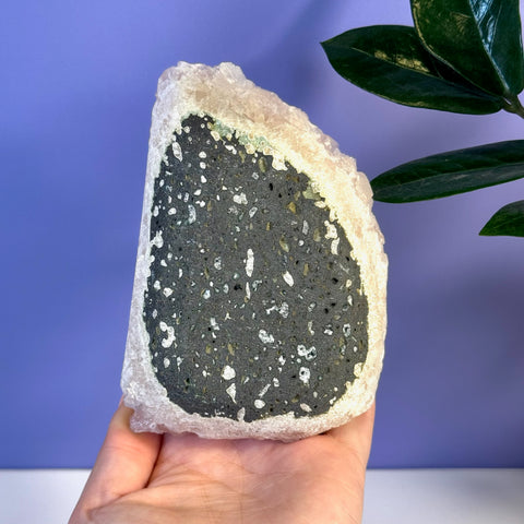 Hand holding a soft pink apophyllite crystal with a dark gray speckled interior.