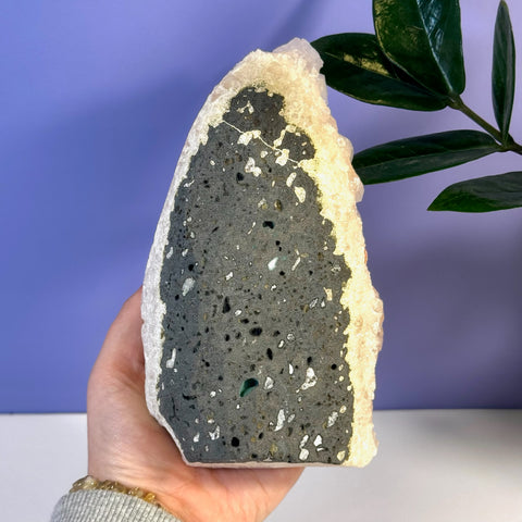 Hand holding a soft pink apophyllite crystal with a dark gray, textured interior and white flecks.