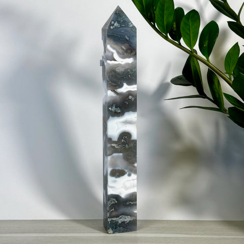 Tall, polished moss agate tower with white, grey, and black swirling patterns, next to a green plant.