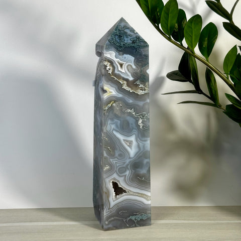 Tall, polished moss agate tower with swirling gray, white, and green patterns, featuring a small geode opening.