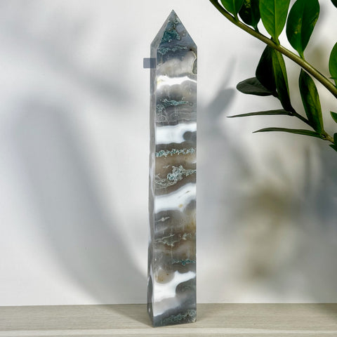 Tall, polished moss agate tower with white, gray, and green swirling patterns, standing on a light wood surface.