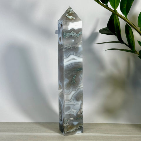 Tall, polished moss agate tower with swirling white, gray, and green patterns, against a white wall.