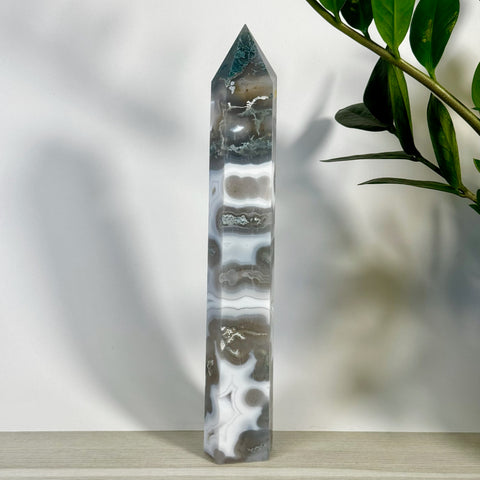 Tall, polished moss agate tower with white, grey, and dark green swirling patterns, next to a green plant.